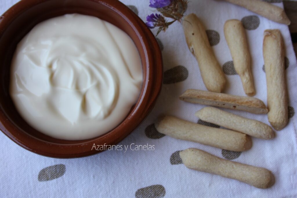 Receta de mayonesa casera clásica:cazuela de barro con mayonesa casera y unos roscos de pan. Un poco de flor de lavanda acompaña a la imagen.