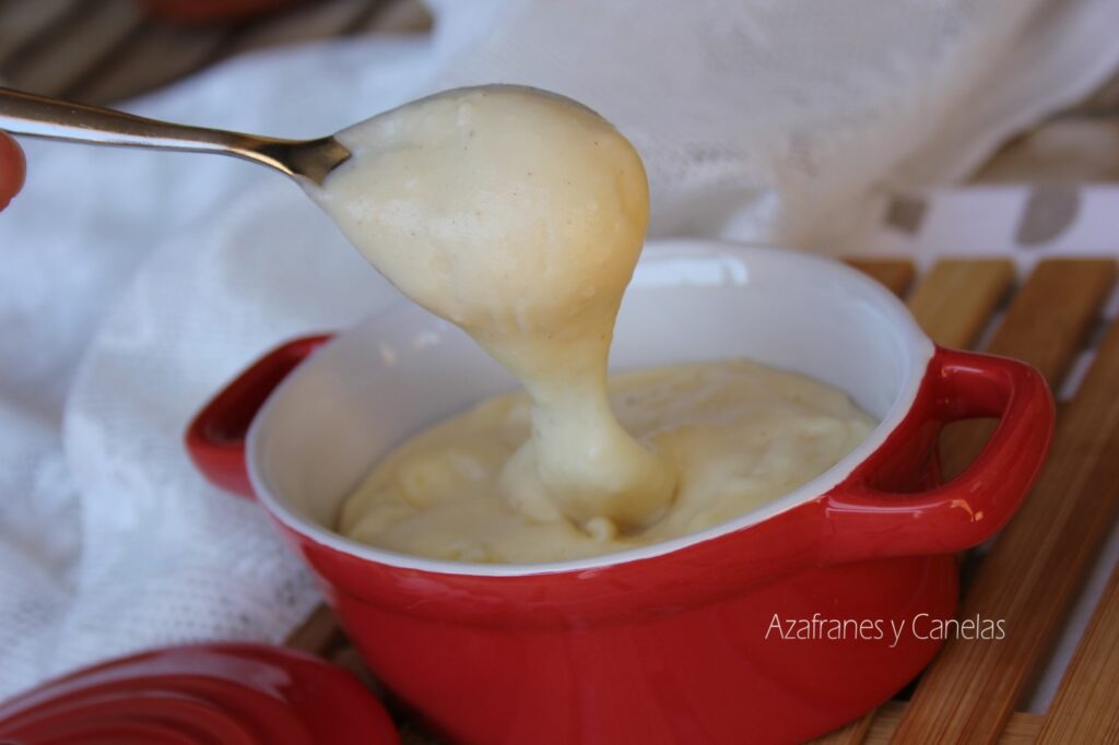 Salsa Bechamel: trucos para que quede perfecta. Ollita con salsa bechamel blanca y suave. Una cuchara toma parte de la salsa caliente y humeante.