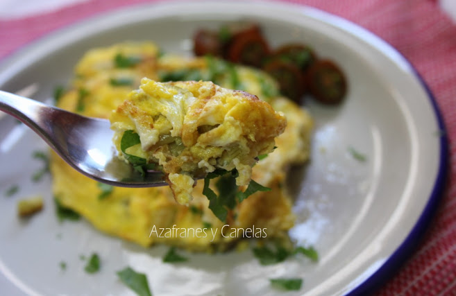 Tortilla de bacalao con patatas. en un plato de cerámica con tomates pequeños aliñados. Un tenedor sujeta un trozo de la tortilla.